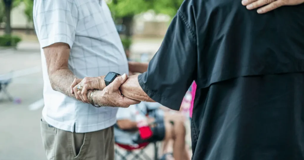 Äldre man håller en äldre persons hand som har en svart smartklocka på handleden.