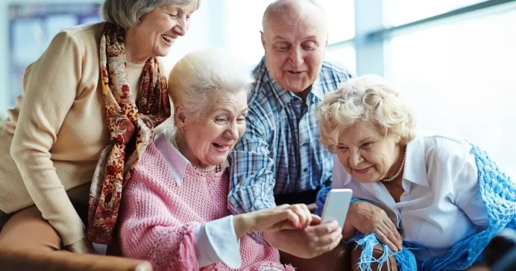 Fyra glada seniorer sitter tillsammans och tittar på en smartphone.