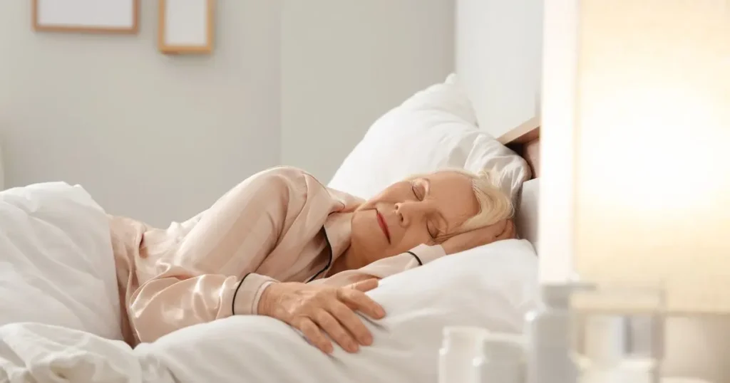 Äldre kvinna med blont hår sover fridfullt i en säng med vit sängkläder.